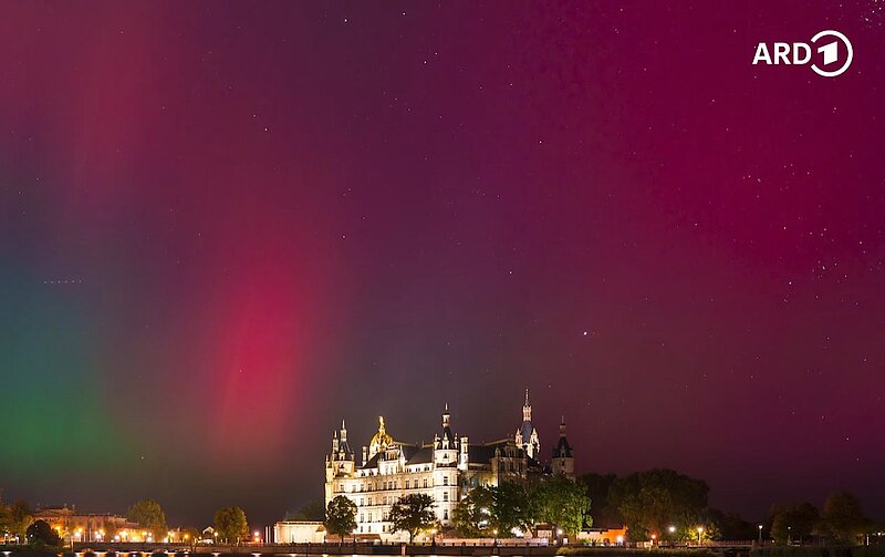 Durch Polarlichter lila-rot und grün gefärbter Stadt-Himmel