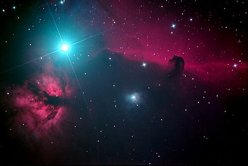 Pferdekopf- und Flammennebel vor in schwarzen und rötlichen Farben mit Orions weißblau leuchtendem Gürtelstern Alnitak